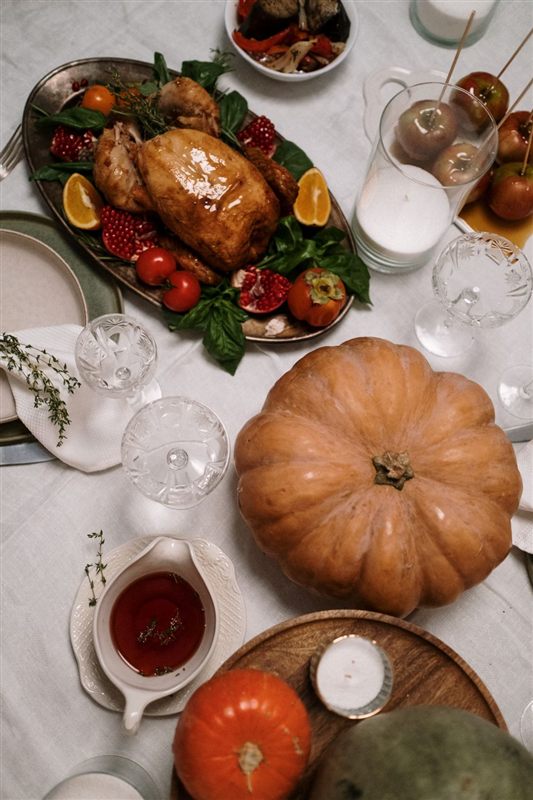 A roast turkey on a serving platter surrounded by tomatoes and orange slices beside a pumpkin