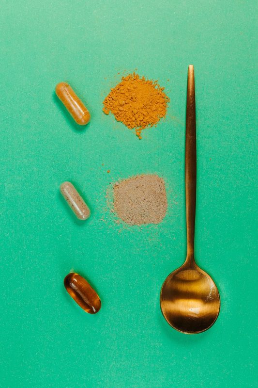 Herbal capsules and powders arranged next to a spoon on a green background