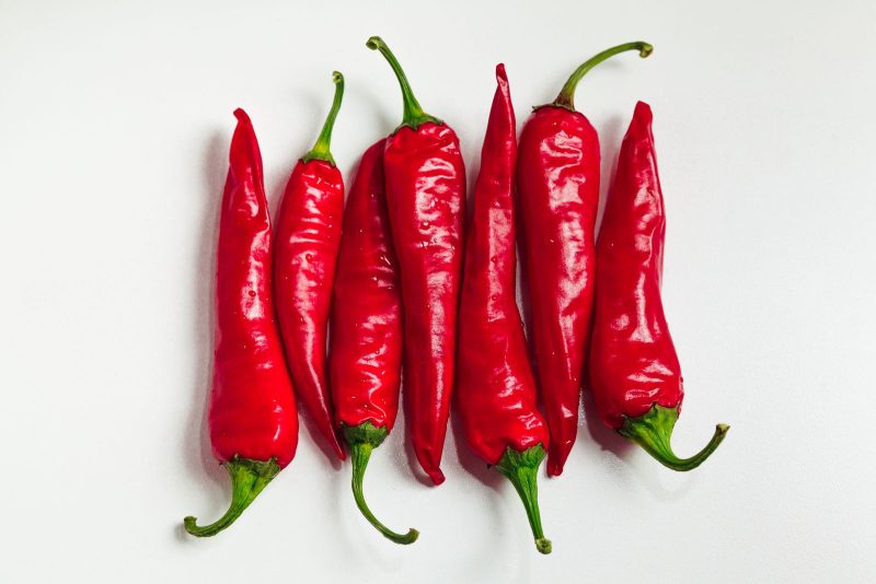 Fresh red cayenne peppers laid side by side on a white surface
