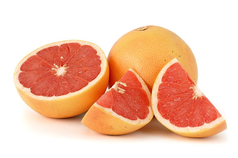 A pink grapefruit cut in half beside a whole grapefruit and a wedge