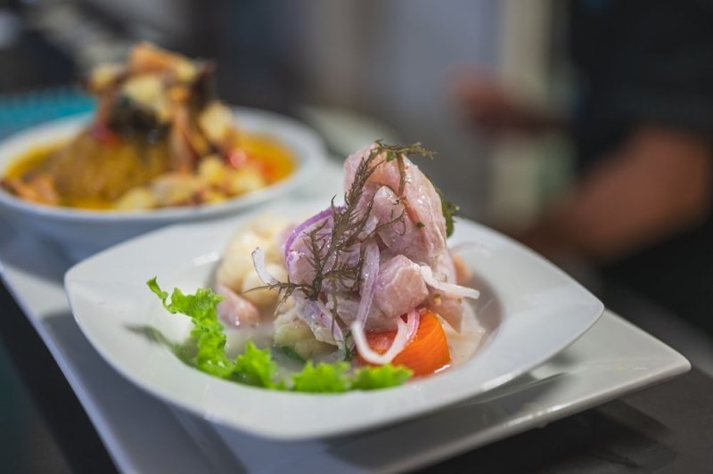 A plate of ceviche with white fish, red onion, and herbs