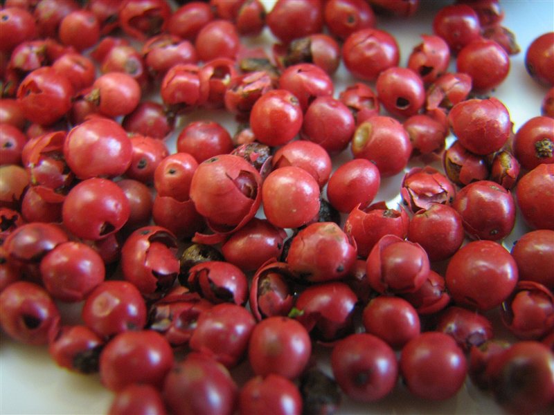 A pile of bright pink-red peppercorns, some with papery husks split open