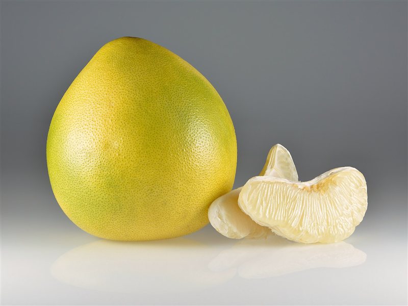 A whole yellow pomelo beside a peeled wedge of pomelo flesh